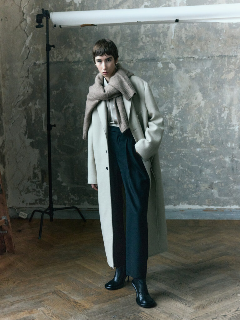 ARTELIER AW26 campaign: female model in a pale coat, scarf and dark trousers